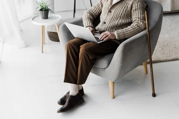 Cropped view of senior man in glasses using laptop while sitting with crossed legs — Stock Photo