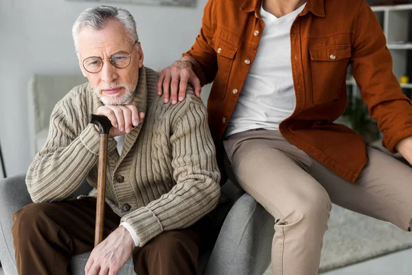 Cropped view of son putting hand on shoulder of sad senior father in glasses — Stock Photo