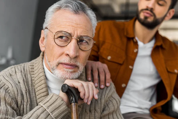 Vue recadrée du fils mettant la main sur l'épaule du père aîné bouleversé dans des lunettes — Photo de stock