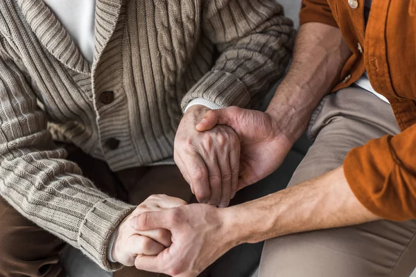 Cropped view of senior father and son holding hands — Stock Photo