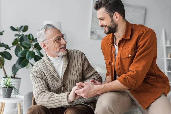 Happy senior father in glasses holding hands with handsome son at home — Stock Photo