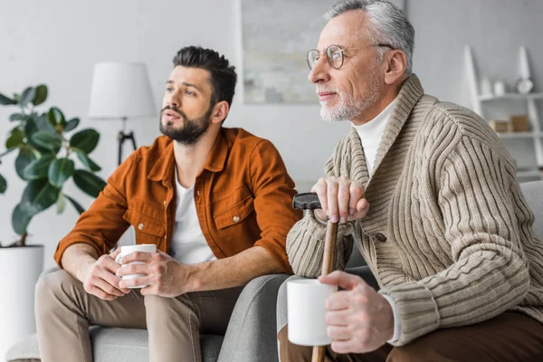 Cheerful retired man in glasses sitting handsome son and holding cup — Stock Photo