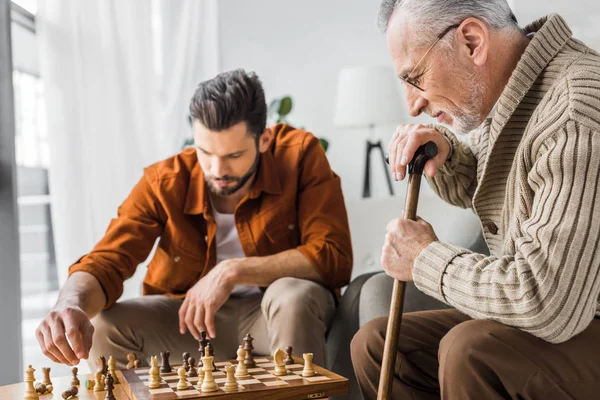 Enfoque selectivo de padre mayor en gafas jugando ajedrez con hijo - foto de stock