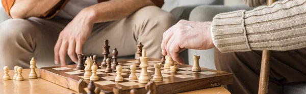 Tiro panorámico de padre e hijo jubilados jugando ajedrez en casa - foto de stock