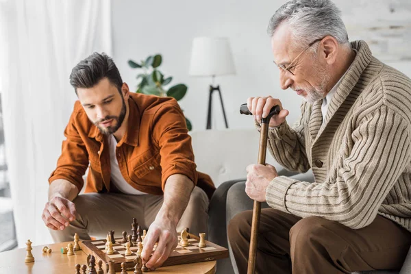 Padre mayor en gafas jugando ajedrez con hijo en casa - foto de stock