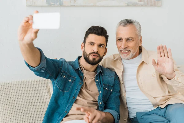 Handsome bearded man taking selfie with senior father at home — Stock Photo