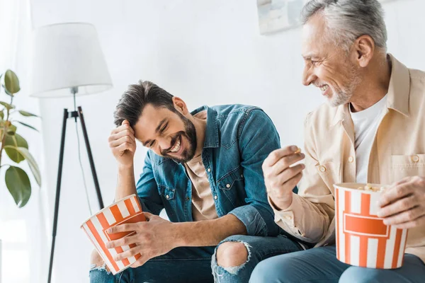 Щасливий старший батько сидить зі усміхненим сином і тримає попкорн відро — стокове фото