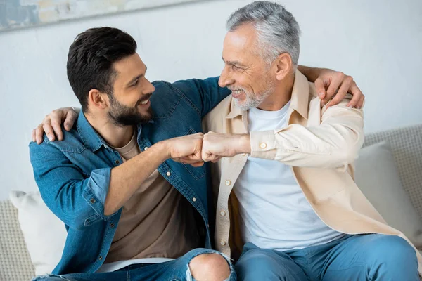 Cheerful retired man fist bumping with happy bearded son at home — Stock Photo