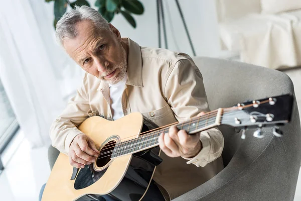 Senior uomo suonare la chitarra acustica e guardando la fotocamera — Foto stock