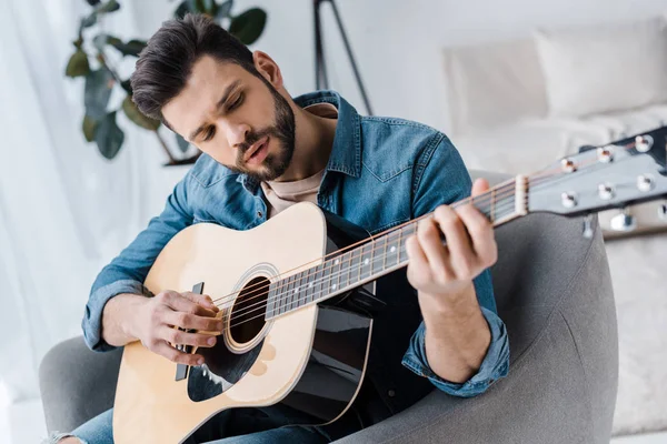 Красивый бородатый мужчина играет на акустической гитаре дома — стоковое фото