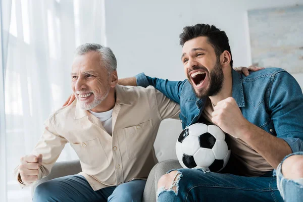 Feliz hombre retirado viendo el campeonato y animando con hijo guapo celebración de fútbol - foto de stock