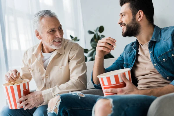 Felice padre in pensione guardando il figlio e tenendo secchio popcorn a casa — Foto stock
