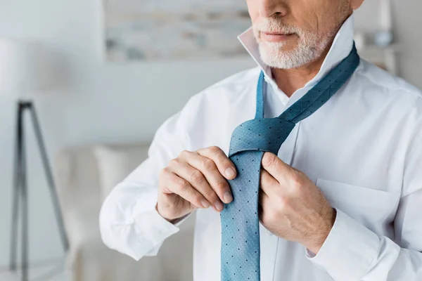 Обрезанный вид уверенного и элегантного пожилого человека, связывающего галстук дома — стоковое фото
