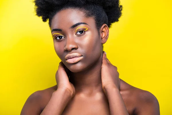 Attraente donna africana americana con trucco alla moda guardando la fotocamera isolata sul giallo — Foto stock