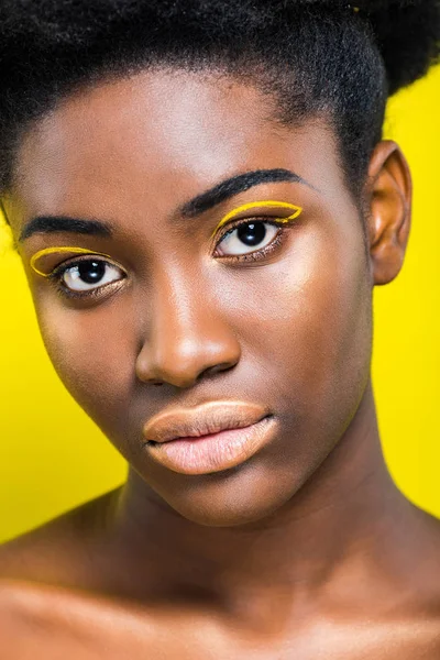 Attraente donna africana americana con trucco alla moda guardando la fotocamera isolata sul giallo — Foto stock