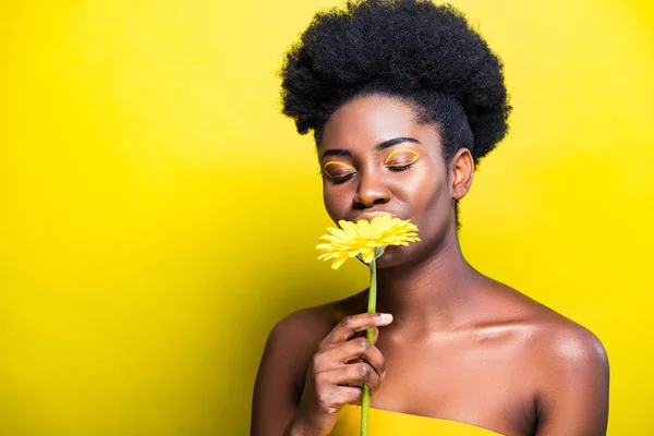 Superbe femme afro-américaine reniflant fleur avec les yeux fermés sur jaune — Photo de stock