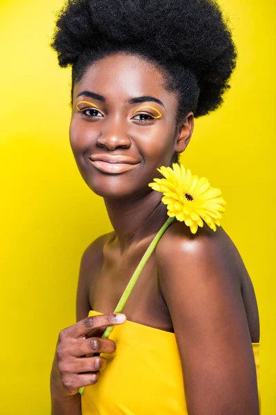 Lächelnde afrikanische Amerikanerin mit Blume auf gelbem Grund — Stockfoto