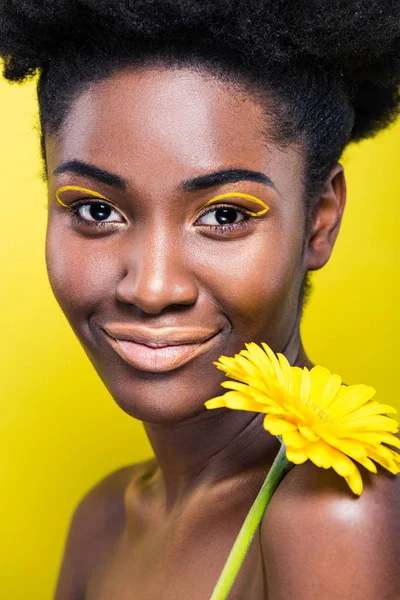 Smiling african american girl holding flower isolated on yellow — Stock Photo