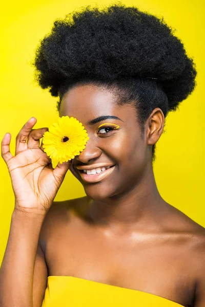 Sonriente chica afroamericana sosteniendo flor aislada en amarillo - foto de stock