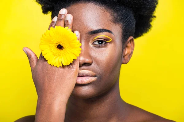 Chica afroamericana seria con flor mirando a la cámara aislada en amarillo - foto de stock