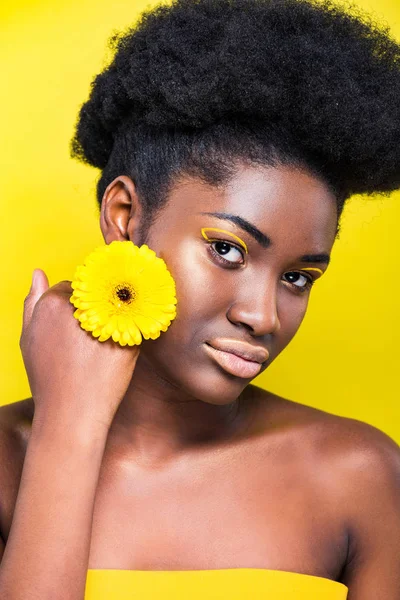Serious african american girl with flower looking at camera isolated on yellow — Stock Photo