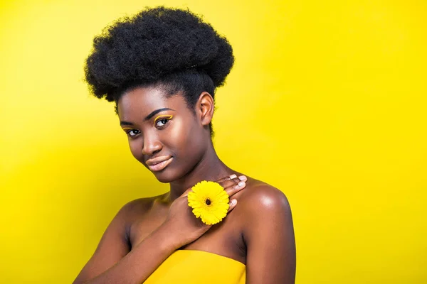 Bastante africana americana chica con flor mirando a cámara en amarillo - foto de stock