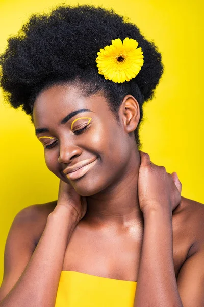 Lächelnd schöne afrikanisch-amerikanische Frau mit Blume isoliert auf gelb — Stockfoto