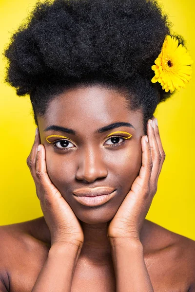 Vista frontal de chica afroamericana bonita con flor en el pelo aislado en amarillo - foto de stock