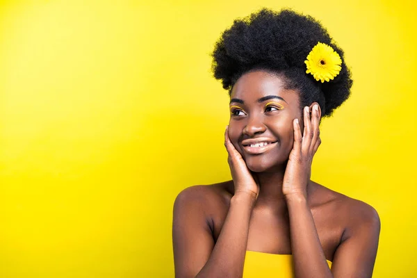 Cheerful smiling african american woman with flower on yellow — Stock Photo