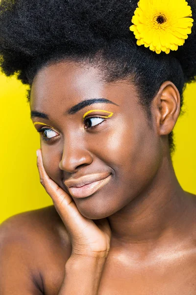 Femme africaine américaine rêveuse avec fleur dans les cheveux regardant loin isolé sur jaune — Photo de stock