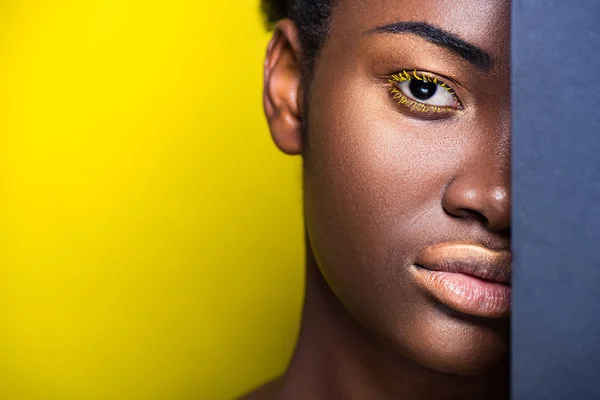 Abgeschnittene Ansicht einer hübschen afrikanisch-amerikanischen Frau mit gelben Wimpern, die in die Kamera auf gelb schaut — Stockfoto