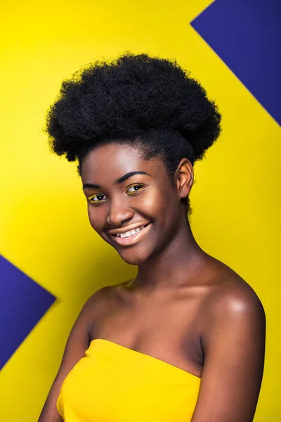 Улыбаясь, довольно африканская американка смотрит в камеру на желтом и фиолетовом — стоковое фото