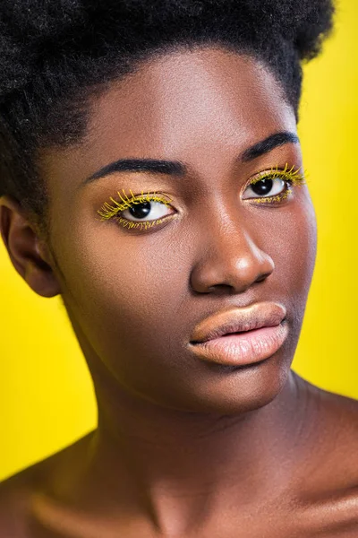 Красива афроамериканська жінка з яскравими віями дивиться на камеру ізольовано на жовтому — стокове фото