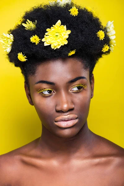 Chica afroamericana pensativa con flores en el pelo mirando hacia otro lado en amarillo - foto de stock