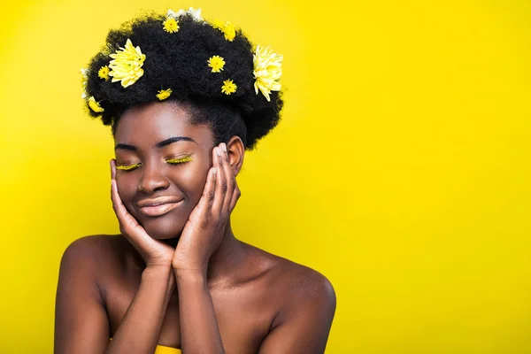 Relajada chica afroamericana con crisantemos en el pelo con los ojos cerrados aislados en amarillo - foto de stock