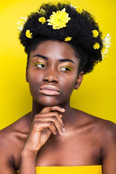 Ragazza afroamericana pensierosa con i fiori nei capelli guardando altrove sul giallo — Foto stock