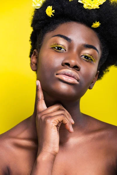 Красива афроамериканська жінка з квітами у волоссі дивиться на камеру ізольовано на жовтому — стокове фото