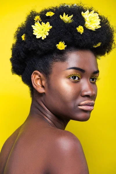 Hermosa mujer afroamericana con crisantemos en pelo aislado en amarillo - foto de stock
