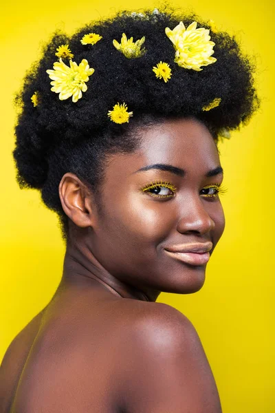 Beautiful african american woman with chrysanthemums in hair isolated on yellow — Stock Photo