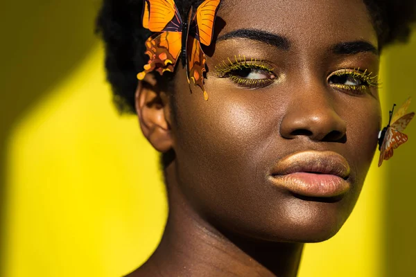 Pensativo afroamericano chica con mariposas mirando hacia otro lado en amarillo - foto de stock