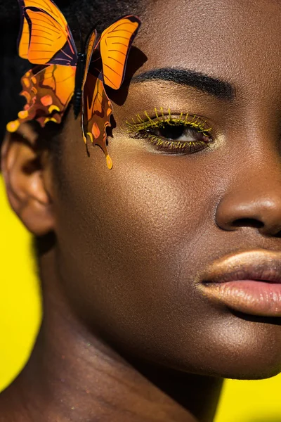 Vue recadrée de fille afro-américaine avec papillon regardant la caméra sur jaune — Photo de stock