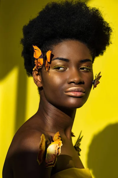 Приваблива афроамериканська молода жінка з метеликами на жовтому — стокове фото