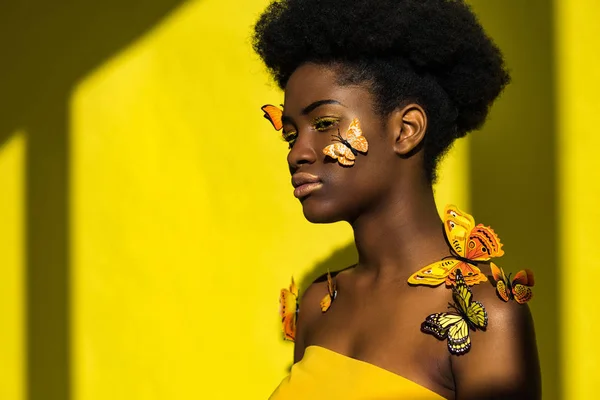 Привлекательная африканская молодая женщина с бабочками на желтом — стоковое фото