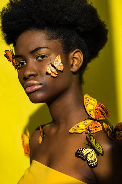 Atractiva joven afroamericana con mariposas en amarillo - foto de stock