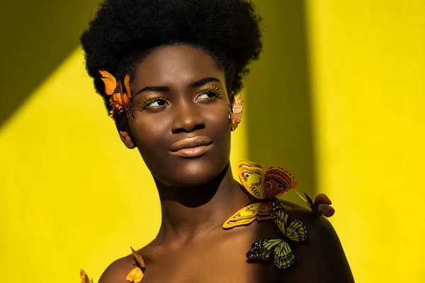 Smiling pretty african american woman with butterflies on yellow — Stock Photo