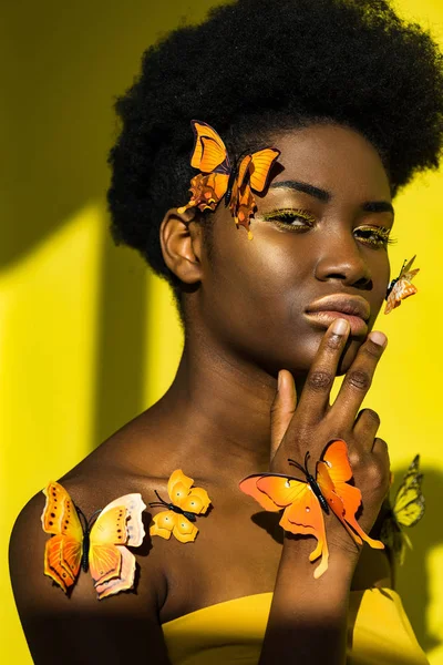 Pensive pretty african american woman with butterflies on yellow — Stock Photo