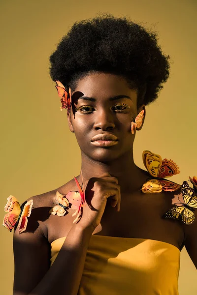 Mujer afroamericana segura con mariposas aisladas en marrón - foto de stock