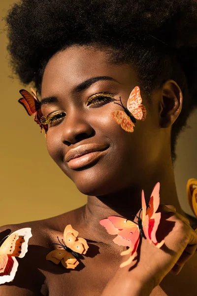 Mujer afroamericana sonriente con mariposas aisladas en marrón - foto de stock