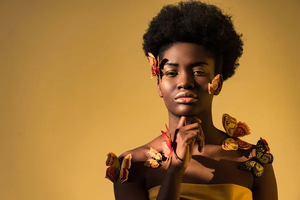 Pensive femme afro-américaine avec des papillons regardant la caméra sur brun — Photo de stock