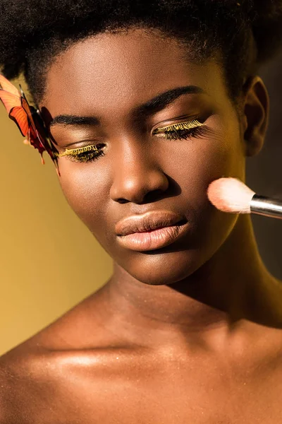 Hermosa mujer afroamericana con mariposa y cepillo de maquillaje en marrón - foto de stock